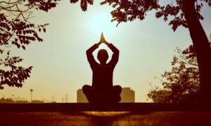 Silhouette of a person practicing yoga outdoors during sunrise, creating a calming atmosphere.