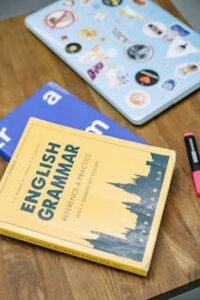 High-angle view of an English grammar book and a laptop with stickers on a wooden desk.